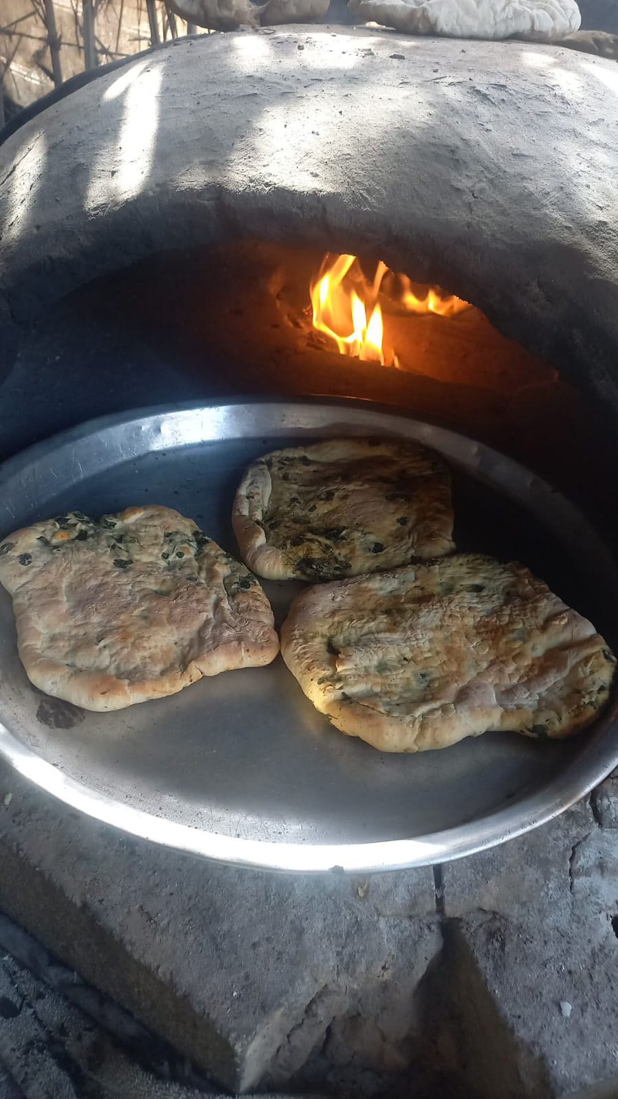 Mona Zahed bakes spinach mahwi in a clay oven, continuing to cook in a tent in Gaza in March 2024 after having been displaced by Israeli attacks.